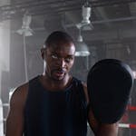A dedicated boxing trainer holding a pad during a gym session.